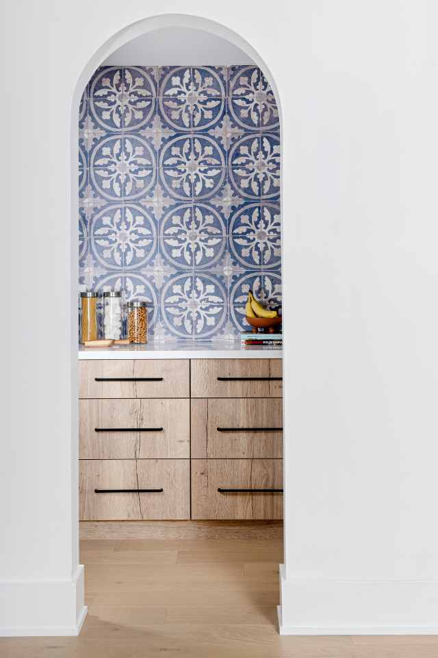 open archway in white wall leading to butler's pantry with blue mosaic tile backsplash behind counter